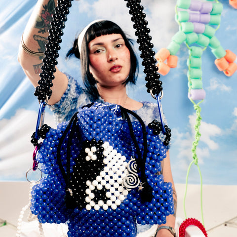 Person holding a blue beaded bag with a yin-yang design against a colorful background.