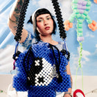 Person holding a blue beaded bag with a yin-yang design against a colorful background.
