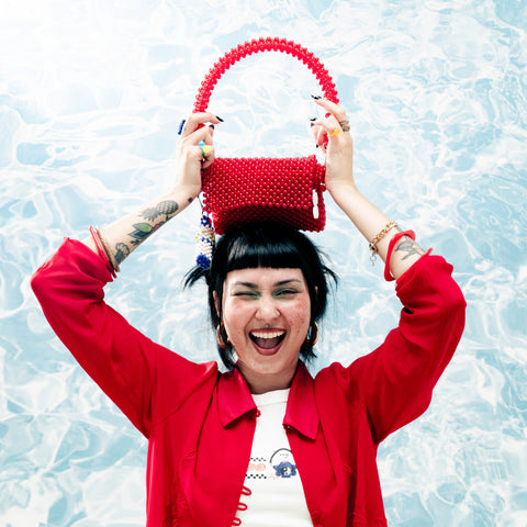 Person wearing a red jacket holding a red beaded bag against a light blue background