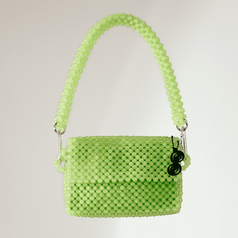 Green woven handbag on a silver pedestal against a light gray background